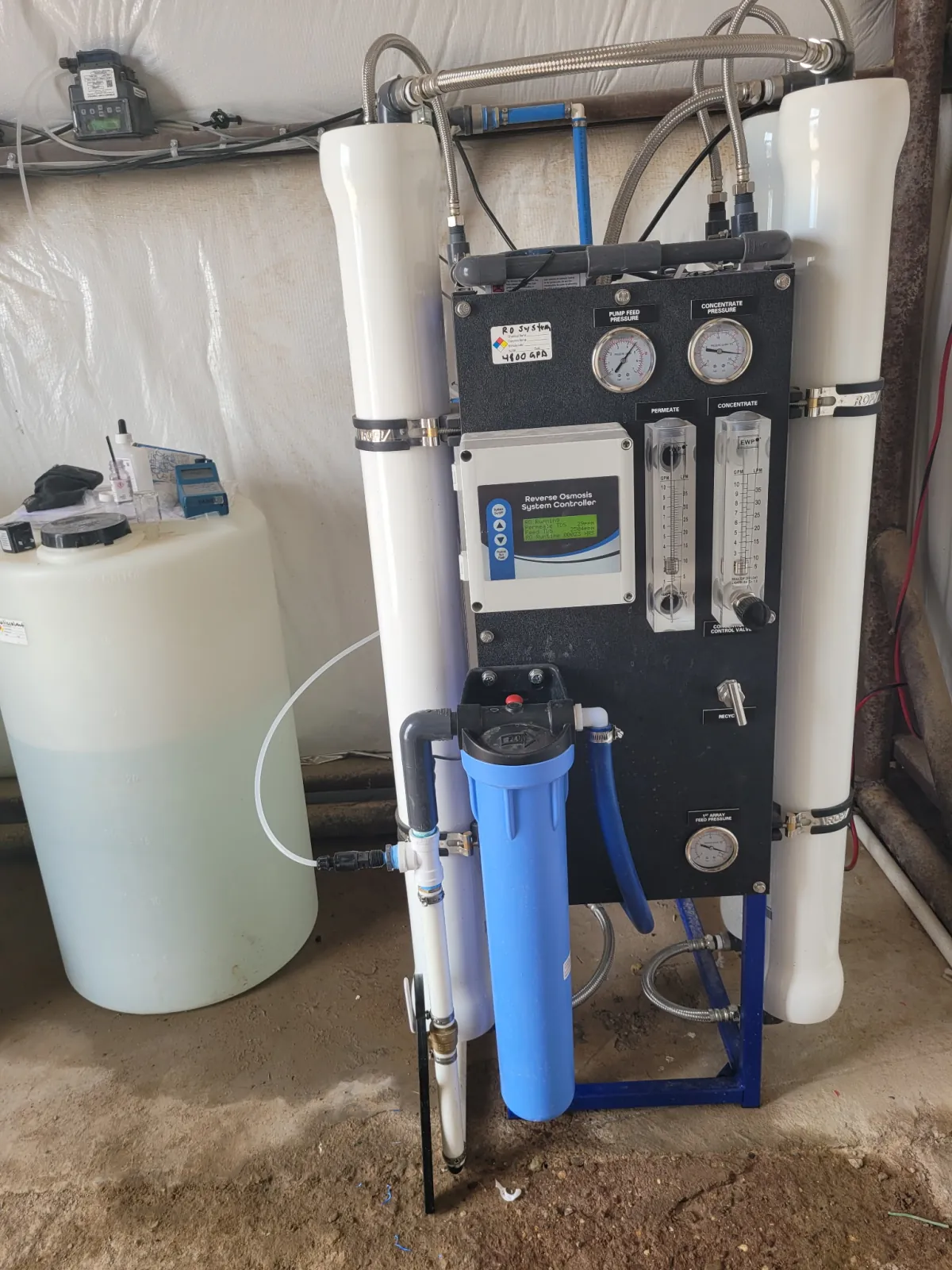 Front view of a commercial reverse osmosis skid with membrane housings, controller, gauges, flow meters, and chemical feed tank
